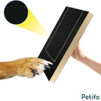 Demonstration graphic of a dog's paw scratching against the textured surface of the black Petifo wooden dog scratch board, held by a person's hand.