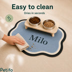 Human hand easily wiping clean a personalized blue cloud-shaped pet feeding mat with a damp cloth.