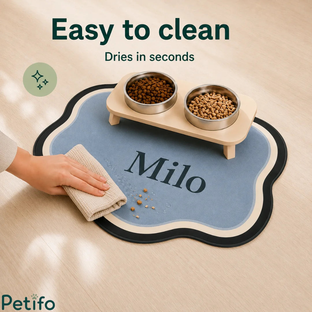 Human hand easily wiping clean a personalized blue cloud-shaped pet feeding mat with a damp cloth.