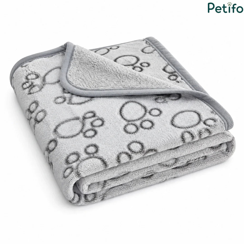 Angled view of a folded grey and white paw print pet blanket resting on a clean white surface.