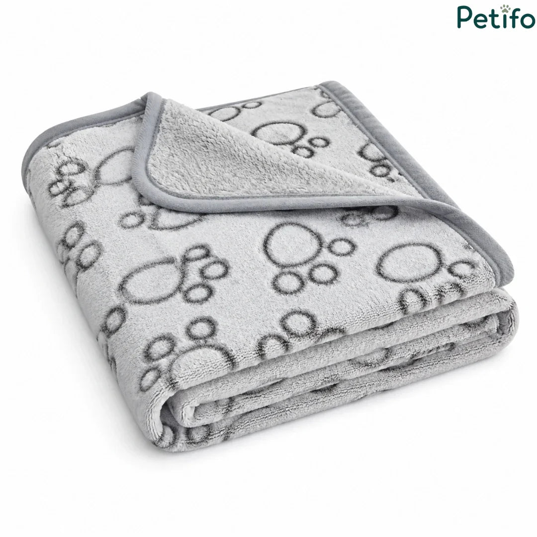 Angled view of a folded grey and white paw print pet blanket resting on a clean white surface.