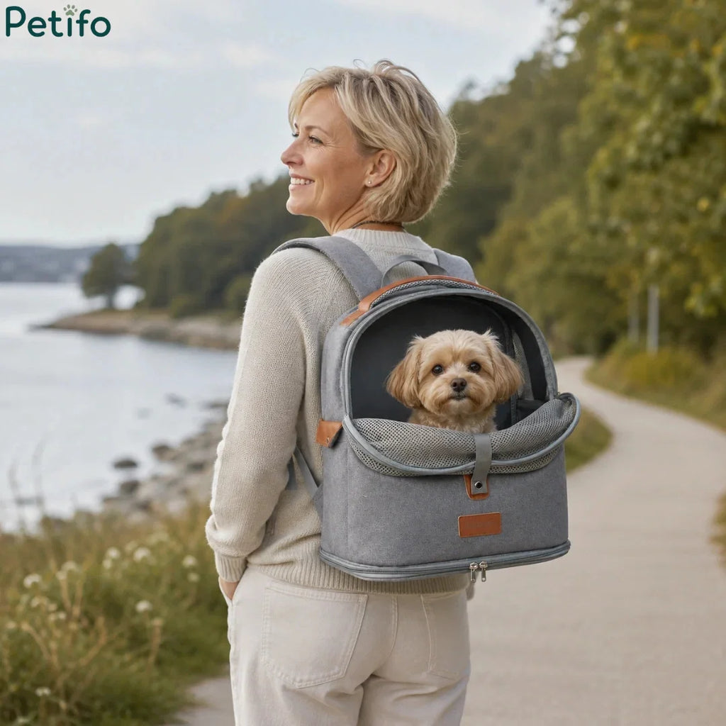 Woman walking outdoors along a scenic waterfront path while wearing a grey pet travel backpack with her small dog inside.