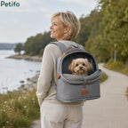 Woman walking outdoors along a scenic waterfront path while wearing a grey pet travel backpack with her small dog inside.