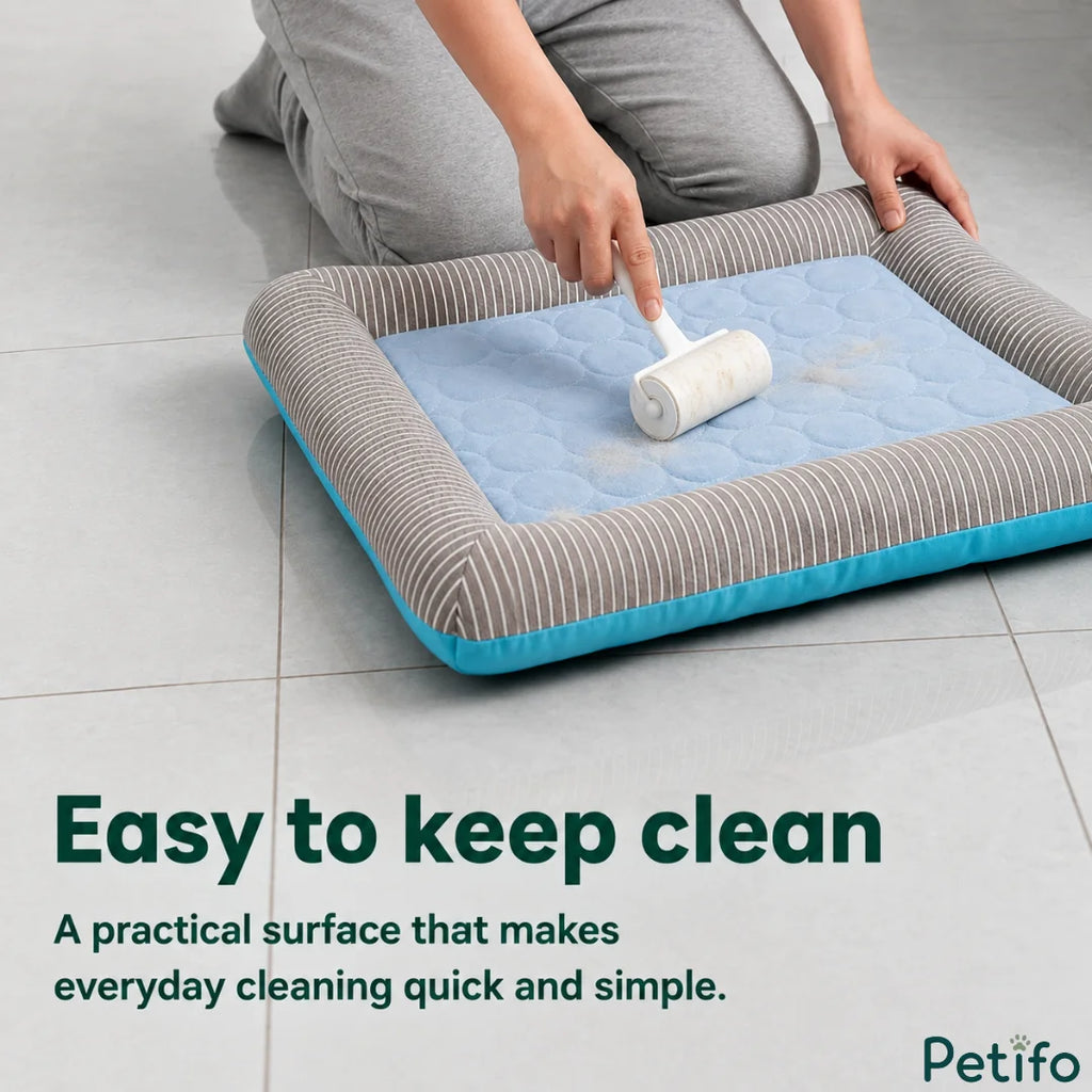 A person using a lint roller to clean pet hair off the surface of a blue and grey striped cooling pet bed.