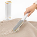 Hand holding a white and gold lint remover brush next to its matching self-cleaning base while removing lint from a beige sweater.